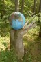 Im Wald steht eine große Hand aus Holz, darin eine mit einer Weltkarte bemalte Holzkugel