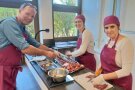 Ein Mann und zwei Frauen schneiden Fleisch am Küchentresen