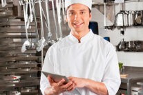 Koch steht in der Küche und hat Tablet in der Hand zur Kalkulation