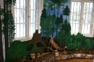 Ausstellungsraum mit gemalten Waldwandbild und Präperaten am Boden