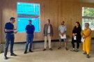 sechs Personen stehen in einem neu gebauten Holzgebäude und unterhalten sich im halb Kreis