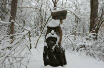 geschnitzte Holzfigur mit einem Grüß-Gott-Holzschild in der Hand im Winter mit Schnee
