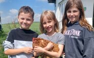 Drei Kinder stehen zusammen mit einem Huhn auf dem Arm